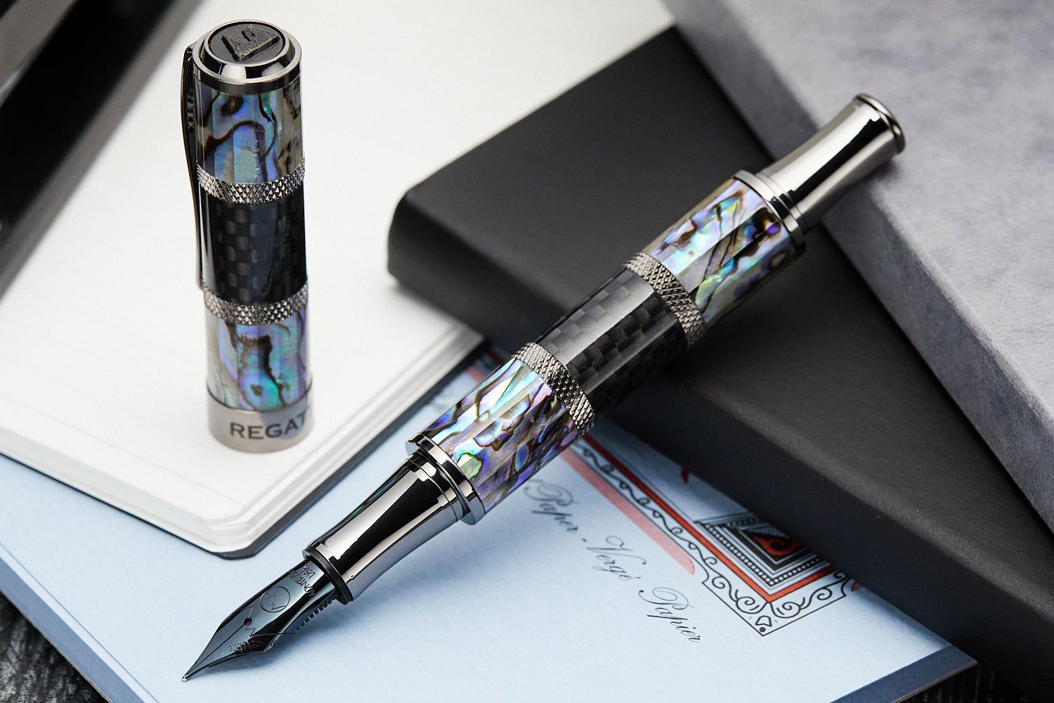 A metal fountain pen with alternating bands of iridescent abalone and black checkered carbon fiber