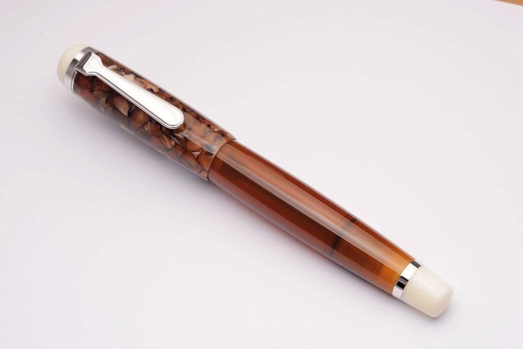A bulbous fountain pen with a transparent brown body, a variegated brown acrylic cap and white ends