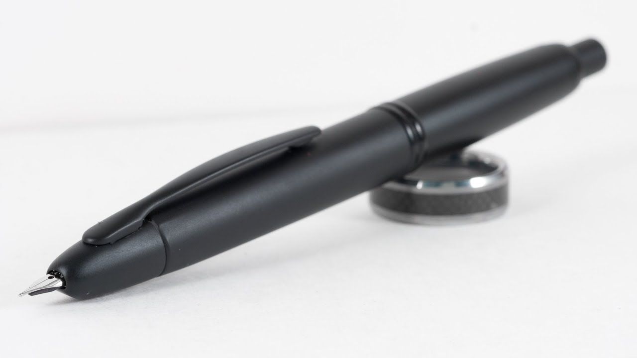 a completely black fountain pen with a button on the back to retract the nib, propped on a ring